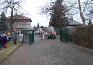 Otworzona brama. Konie ciągnące sanie z Mikołajem wjeżdżają na teren przedszkola.
