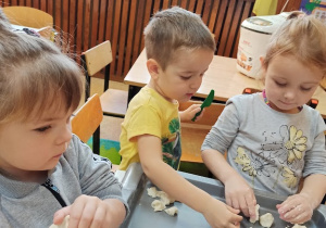 Przy stolikach, na tackach każde z dzieci formuje swoją ulepiankę. Jest rogalik i kule, z któych chyba powstanie bałwanek.