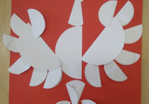 Praca plastyczna. Na dużym czerwonym kartonie orzeł wykonany z różnej wielkości białych kółek z origami.
