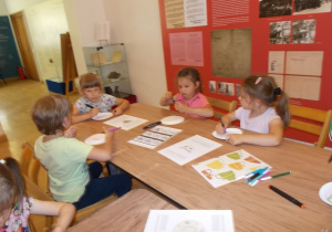 Dzieci siedzą przy stolikach. Na papierowych talerzykach każdy, używając pisaków, projektuje swoje wzory.