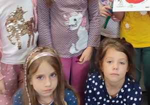 Dziewczynki ubrane w bluzki w różnej wielkości kropki. Jedna trzyma książeczkę z namalowaną pomarańczową kropką.