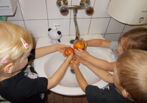 Troje dzieci myje jabłka pod kranem w łazience.