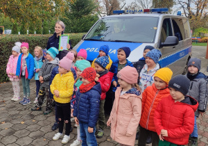 Pamiątkowe zdjęcie przy radiowozie. Pani policjantka trzyma dyplom z podziękowaniem.