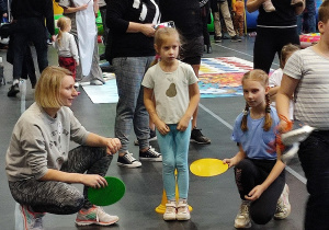 Dziewczynka przechodzi po krążkach a mama z siostrą je kolejno przekładają.