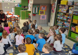 Dzieci siedzą na dywanie i zadają pytania pani z fundacji.