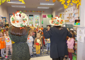 Dwie panie prowadzące w jesiennych kapeluszach na głowie. Przymocowane do nich są kolorowe liście i owoce.
