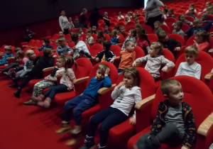 Widownia w teatrze. Dzieci siedzą w rzędach na czerwonych fotelach czekając na przedstawienie.