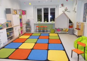 Sala Starszaków. Dywan w kolorową kratę, niskie mebelki, kącik w kształcie domku do odpoczynku z materacem i poduchami.. Na ścianach naklejki kolorowych sów.