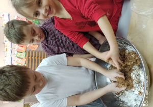 Dwóch chłopców i dziewczynka ugniatają ciasto w misce.