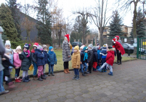 Wszystkie dzieci ubrane stoją na chodniku przed przedszkolem ustawione w szeregu.