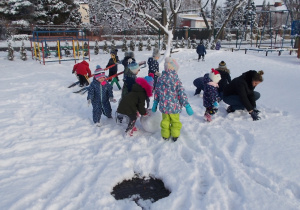 Dzieci w ogrodzie. Pochylają się i lepią śnieżki oraz większe kule.