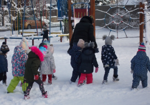 Dzieci za panią idą po śniegu wysoko podnosząc nogi i zostawiając za sobą głębokie ślady.