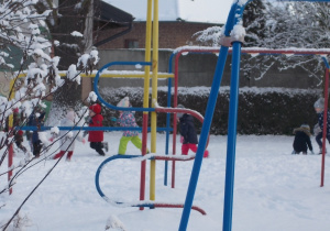 Dzieci biegają po śniegu między urządzeniami terenowymi - drabinkami.