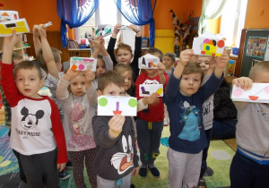 Dzieci podnoszą do góry wykonane ze składanki techniką origami swoje pierwsze portmonetki. Ozdobione są wzorami kolorowych figur.