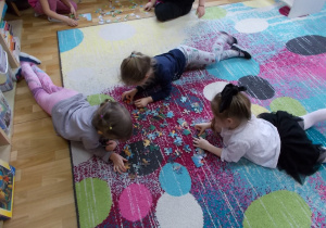 Trzy dziewczynki leżą na dywanie i dopasowują klocki.