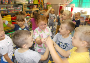 Dzieci uśmiechnięte, w strojach w kolorach jesieni, stoją w grupach dotykając się figurami w kształcie koła.