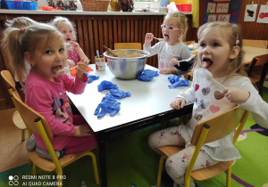 Dzieci siedzą przy stoliku. Próbują powstałą masę przez zlizywanie jej z łyżeczek.