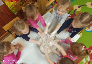 W misce wsypana mąka. Dzieci stoją dookoła i wkładają ręce do miski.