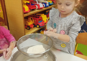 Dziewczynka trzyma sitko i przesiewa mąkę.