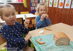 Dziewczynki siedzą przy stole i jedzą upieczony chleb.