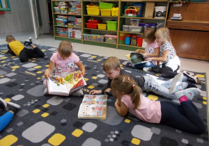 Dzieci siedzą na dywanie. Oglądają sobie książeczki.