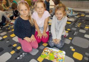 Trzy dziewczynki siedzą na dywanie. Przed nimi ułożone wspólnie puzzle.