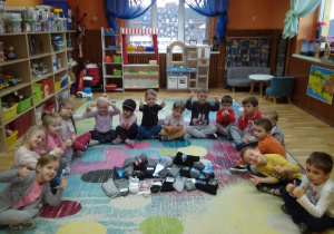Skarpety ułożone na środku dywanu. Dookoła siedzą dzieci, uśmiechają się i wskazują kciuki do góry.