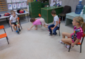 Dzieci pokonują slalom między krzesłami chodząc na czworaka i skacząc obunóż.