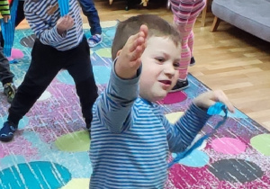Uśmiechnięte dzieci tańczą trzymając kolorowe paski bibuły.
