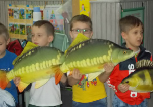 Trzech chłopców. W ich rękach materiałowe sylwety różnych ryb.
