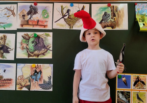 Chłopczyk na głowie ma czapkę z głową bociana. W tle, na tablicy obrazki różnych ptaków.