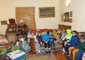 Dzieci w "pokoju babci" siedzą na dawnych ławach, krzesłach, łóżkach. Słuchają bajki "Gąska Balbinka" puszczanej z płyty gramofonowej.