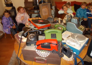 Na środku pokoju okrągły stół a na nim zgromadzone z dawnej epoki różne urządzenia: telefony, gramofony, kasy sklepowe ....