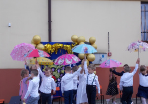 Dzieci tańczą w parach. Trzymają w górze parasole.
