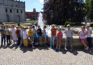 Cała grupa pozuje do zdjęcia w parku przy fontannie.