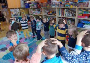 Dzieci stoją w kole. Podczas zabawy ze śpiewem kładą dłonie na głowie kolegi lub koleżanki stojących po obu stronach.