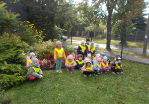Dzieci pozują do zdjęcia przy przedszkolnym skalniaku pełnym jesiennych kwiatów.