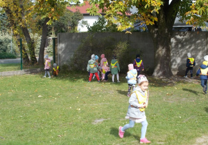 Dzieci biegają po ogrodzie i zbierają liście oraz kasztany.