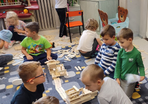 Grupa chłopców siedzi na dywanie. Układają wspólną budowle z drewnianych klocków Maple.