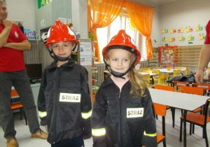 Dwoje dzieci w strojach strażaków.