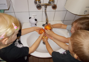Troje dzieci myje jabłka pod kranem w łazience.