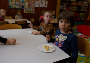 Dzieci siedzą przy stolikach. Przed każdym talerzyk z przygotowaną sałatką.