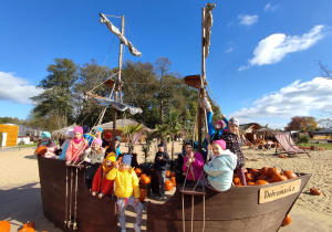 Dzieciaki siedzą w drewnianym statku wypełnionym dyniami.