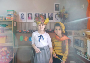 Para dzieci wybrana do konkursu stoi obok siebie. Dziewczynka w wiannku z liści na głowie, chłopiec w kapeluszu i z pędzlem w prawej dłoni.