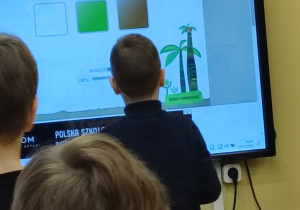 Chłopiec wykonuje zadania na tablicy interaktywnej. Reszta kolegów obserwuje.