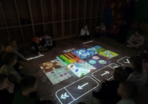 W sali ciemno. Dzieci siedzą na podłodze. Wyświetla się interaktywny dywan.