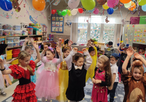 Z sufitu zwisają kolorowe balony i serpentyny. Dzieciaki tańczą po całej sali.