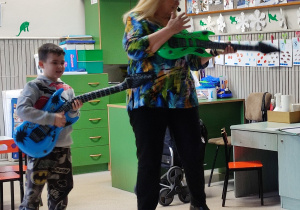 Chłopiec i pani prowadząca grają na dmuchanych gitarach.