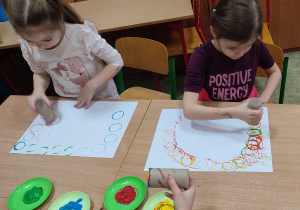 Dzieci siedząc przy stolikach stemplują kolorowe kółka.