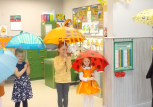 Trzy dziewczynki stoją. Każda trzyma rozłożony nad sobą parasol.